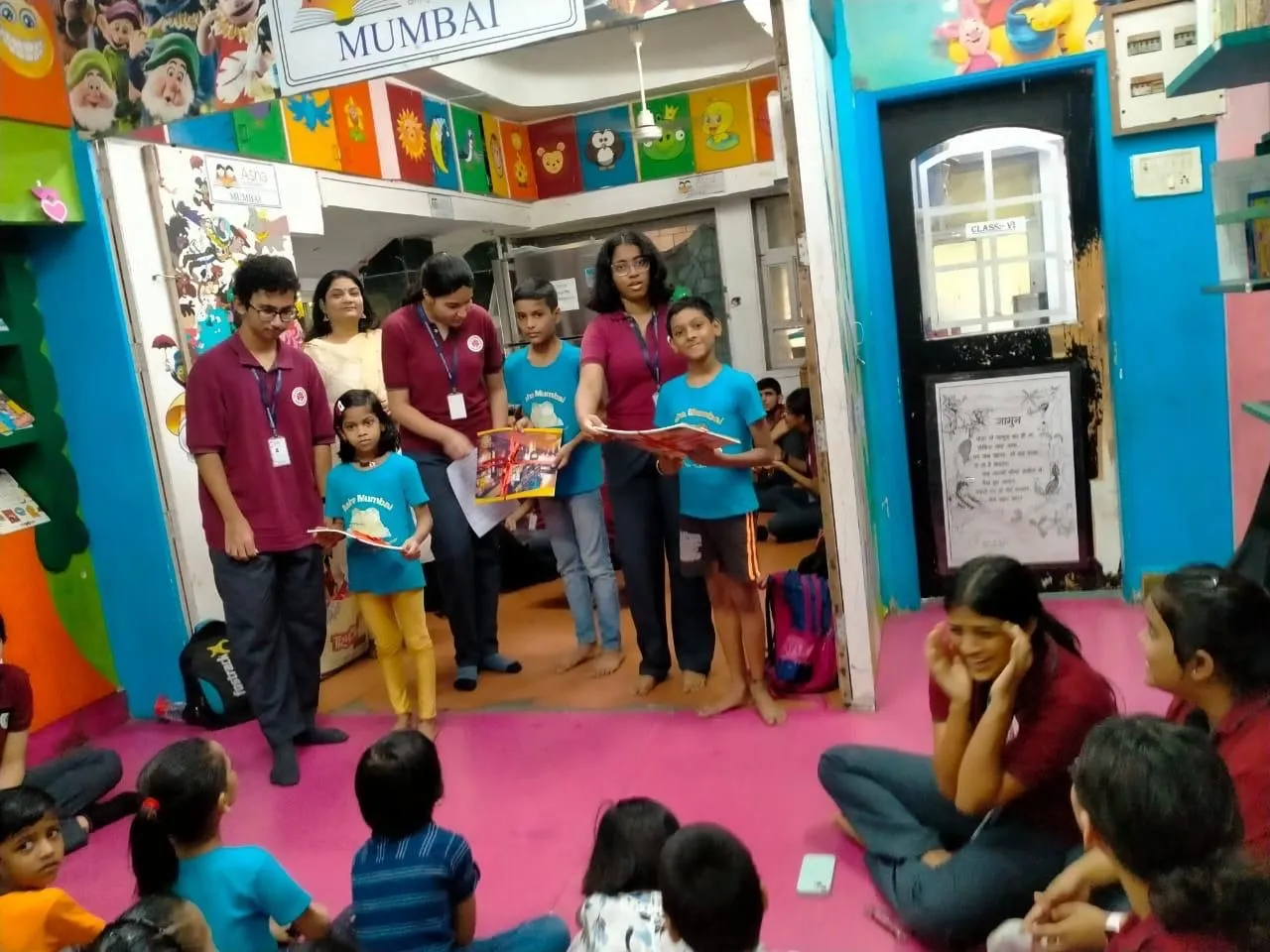Volunteers leading a reading activity with children in a brightly painted classroom, students seated on the floor
