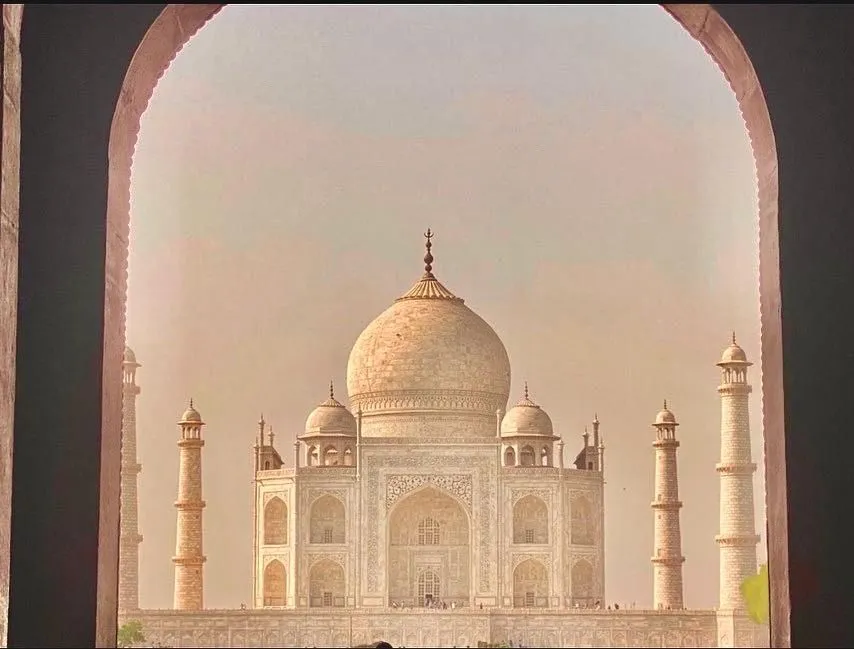 The Taj Mahal framed through a dark arched gateway in warm, hazy light