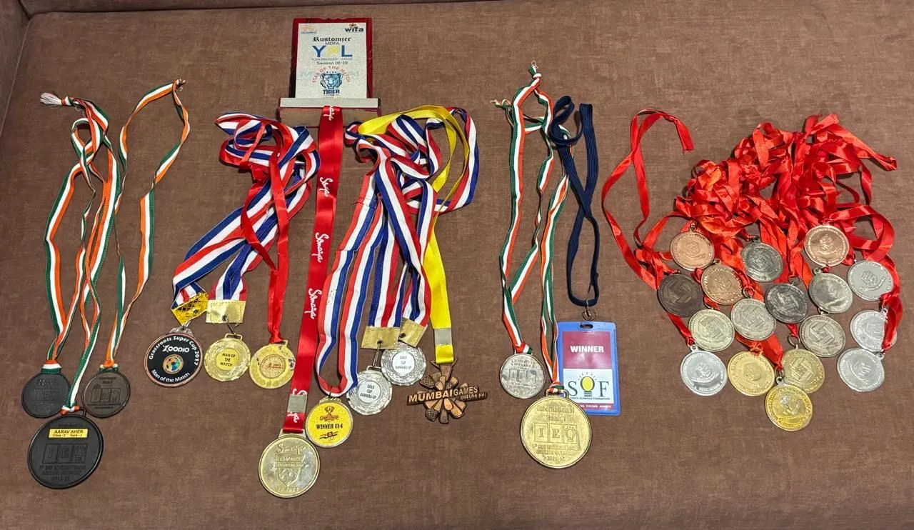 Rows of medals laid out on a sofa, including Man of the Match and U14 winner medals and a Star of the Match trophy